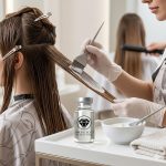 A hairdresser applies a treatment to a client's hair using a brush. Nearby, a small ampule labeled "Diamond Botox Hair Repair Treatment" and a bowl of cream are on the table.