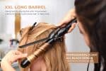 A stylist uses the Ultimate Pro Clip Curling Iron 1" with an XXL long black barrel to curl a client’s blonde hair in a salon, highlighting its professional design and advanced features.