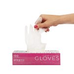 A hand pulls a clear disposable glove from a pink and white box labeled "Clear Deluxe Vinyl Gloves – Powder Free, 100 gloves per box.