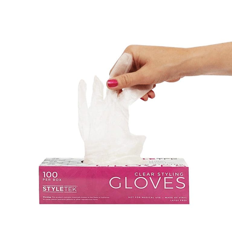 A hand pulls a clear disposable glove from a pink and white box labeled "Clear Deluxe Vinyl Gloves – Powder Free, 100 gloves per box.