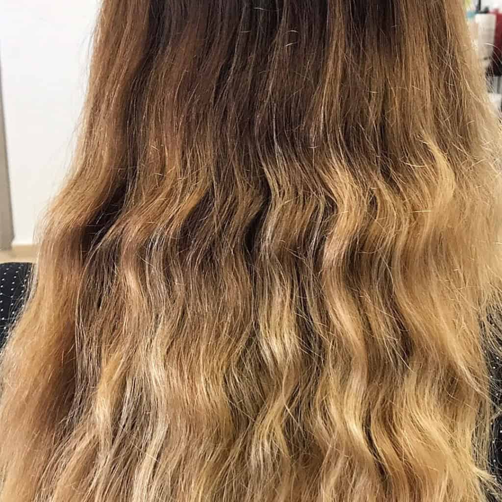 Back view of long, wavy, brown to blonde ombré hair with visible texture and color transition.