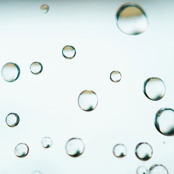 Close-up of several clear water droplets suspended against a light, blurred background.