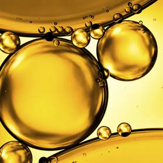 Close-up view of golden-yellow oil droplets suspended in liquid, showing round shapes and varying bubble sizes against a light background.