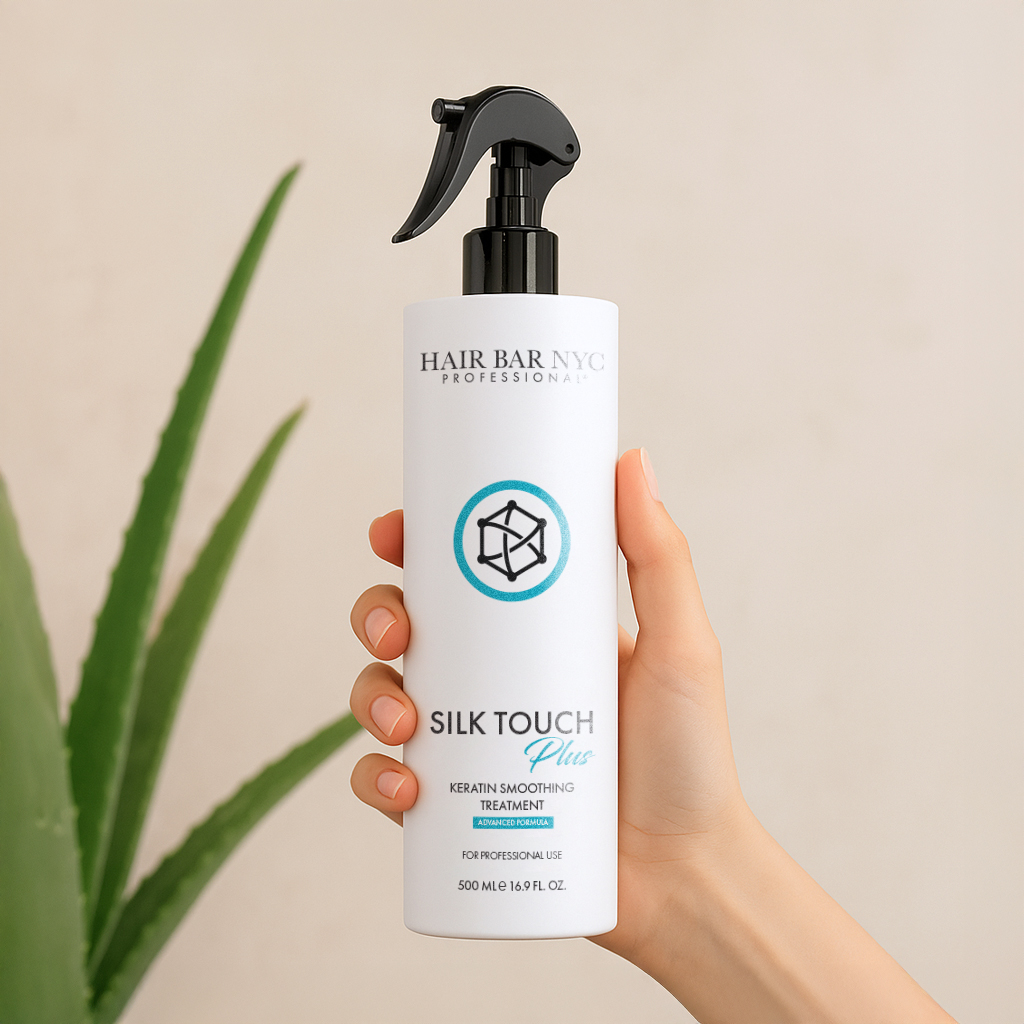 A hand holds a bottle of Silk Touch Plus Keratin Advanced Formula with a spray nozzle, with a green plant in the background.