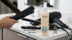 A person straightens hair with a flat iron next to Anti-Frizz Hairspray and a hair dryer on the bathroom counter. Text highlights advanced heat-activated technology for smooth, sleek results.