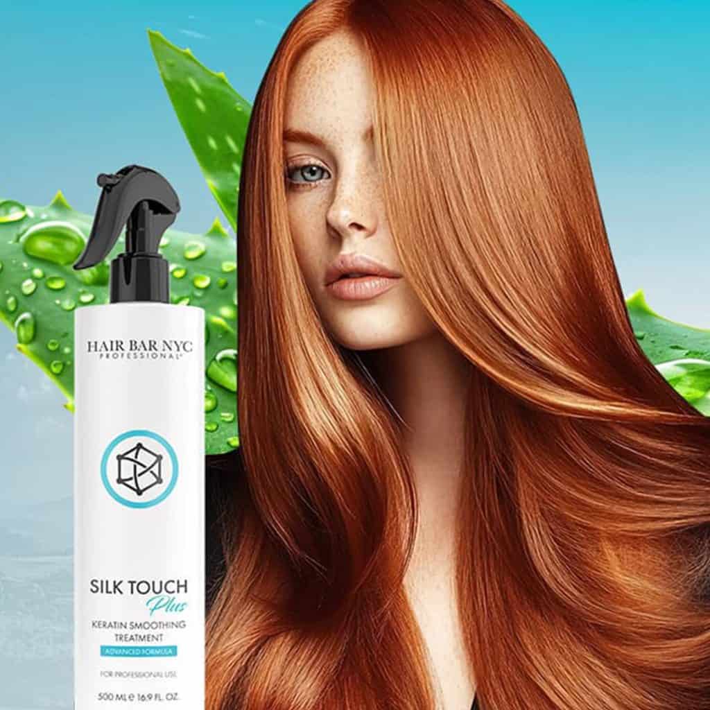 A woman with long, shiny red hair stands next to a bottle of Hair Bar NYC Silk Touch Plus Keratin Smoothing Treatment, with green aloe leaves in the background.